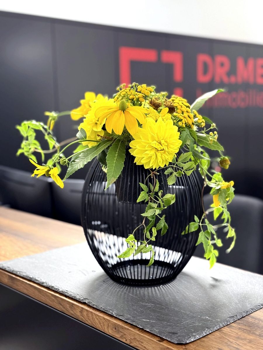 Gelbe Blumen in schwarzer Drahtvase